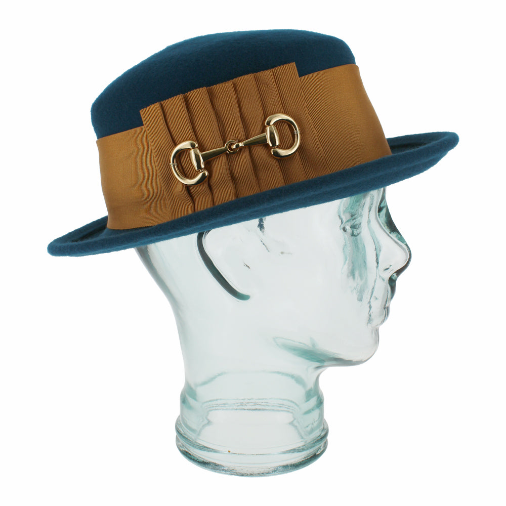 Close-up of the Belfry Gardiner teal blue wool boater hat showcasing its bold grosgrain band and gold bow with links, a chic women’s piece for autumn and winter elegance