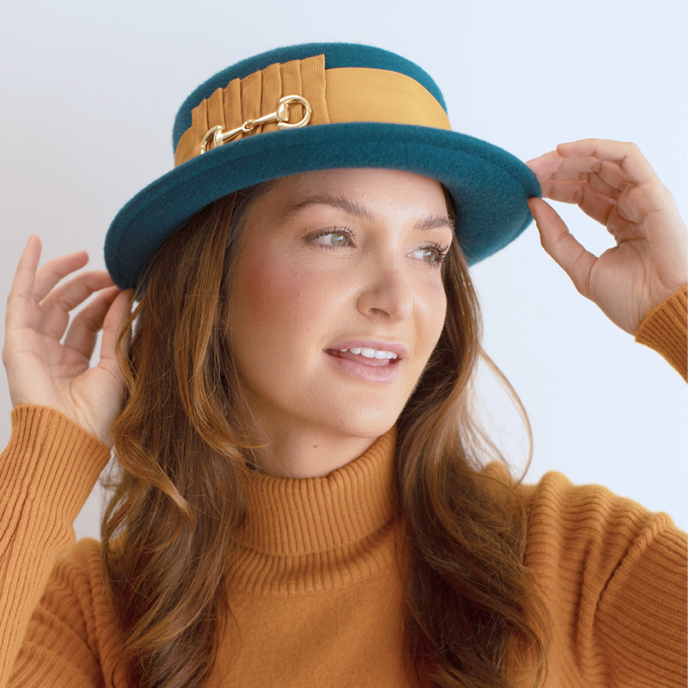 woman wearing a turquoise boater style hat with wide gold band belfry gardiner 